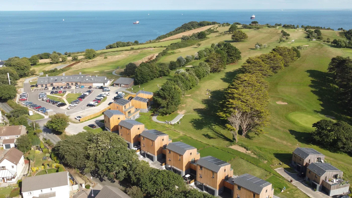 The Green's timber homes beside the fairways of Falmouth Golf Club, with Falmouth Bay beyond